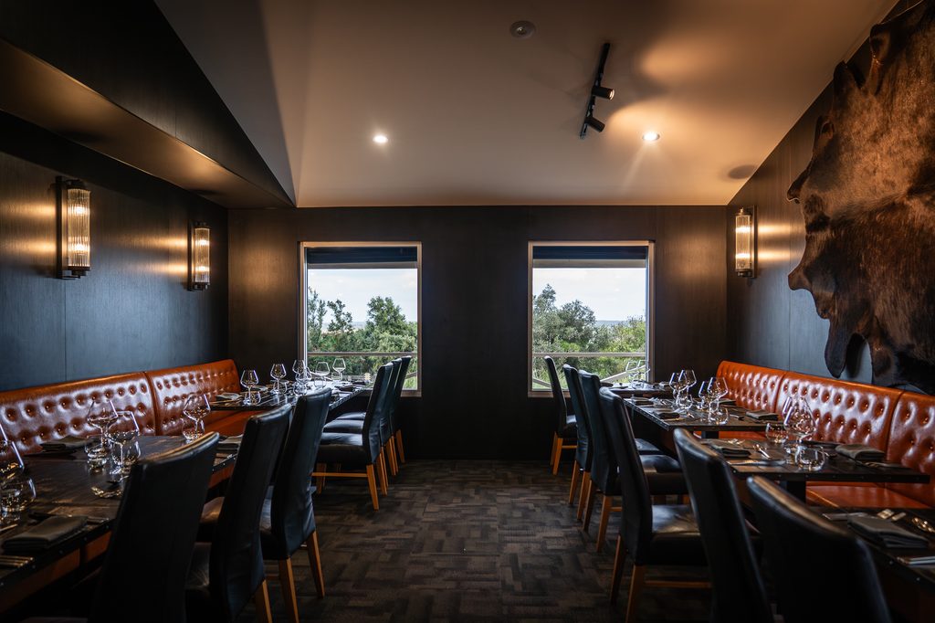 The steakhouse dining room: leather banquettes, set tables, a mounted hide on the wall and two windows onto trees and sky.
